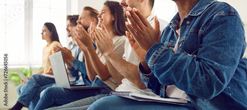 Multiracial audience applauding speaker at business conference or seminar. Happy, satisfied people with laptop PCs and notebooks on lap sitting in row, clapping hands and smiling. Banner background photo