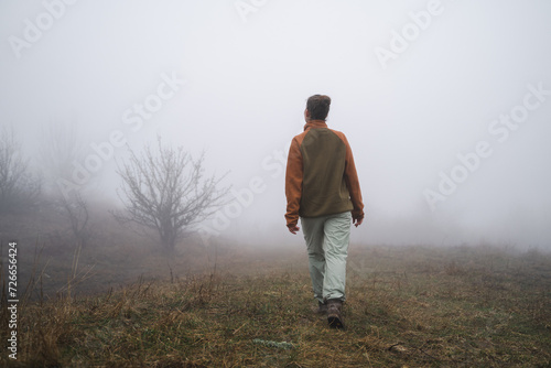 Back view of  young girl hiking traveling going on top of cliff in travel, mountaineer girl goes into the fog, tourist in a foggy field far from civilization, foggy future, without a path photo