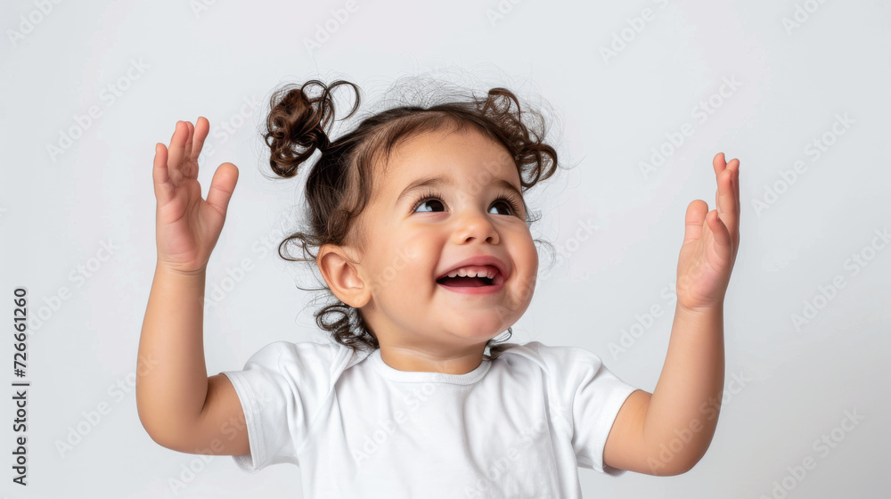 joyful toddler with pigtails is raising her hands in excitement and looking up, set against a plain light background joyful toddler with pigtails is raising her hands in excitement and looking up, set against a plain light background