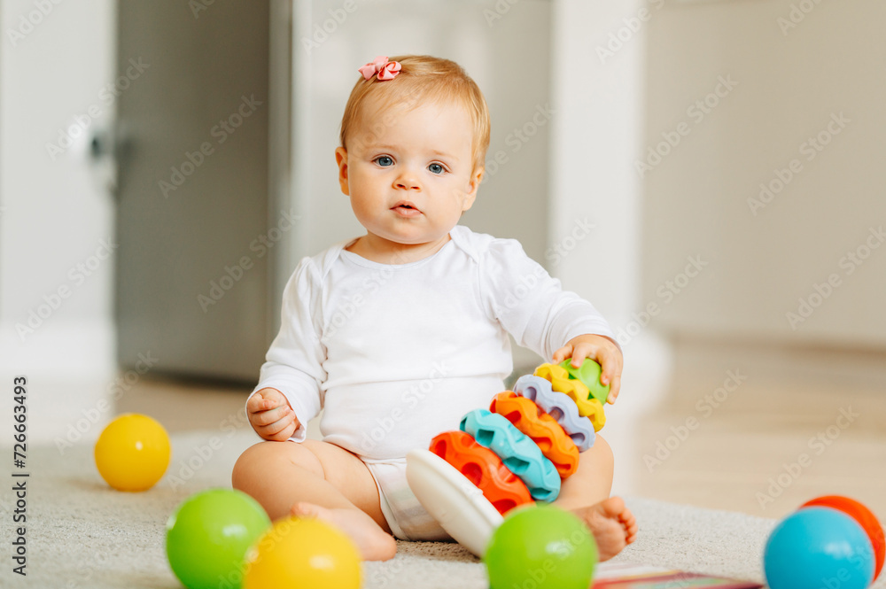 Cute baby girl is sitting on the floor at home while playing with her toys. Cute baby girl is sitting on the floor at home while playing with her toys.