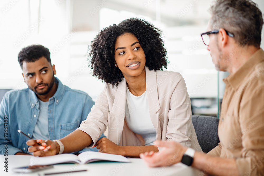 Fototapeta premium Smart and intelligent African-American businesswoman in a white blazer involved in discussion with colleagues, representing a focused work session and effective collaboration in a modern office