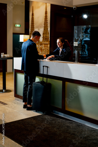 The receptionist at the counter meets the guest with luggage in the hotel business travel hospitality