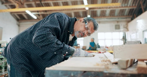 Senior man, carpenter and blowing wood in workshop for dust, shavings or smooth finish at manufacture. Mature male, builder or craftsman working on bench, table or work desk at warehouse or shop