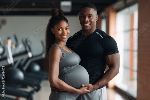 Muscular man and pregnant African American woman in a gym, family couple does sport together