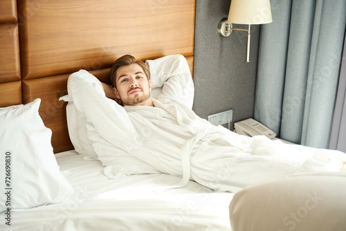 Hotel guest in a bathrobe rests on a large bed