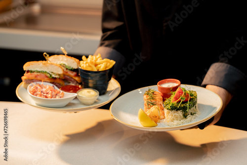 professional kitchen in hotel restaurant close-up chef holds dishes burger and salmon with rice