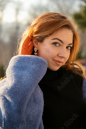 Closeup portrait, posing gorgeous in park, dressed in a orange gloves and blue fur coat, with long red curly hair, sunset background.
