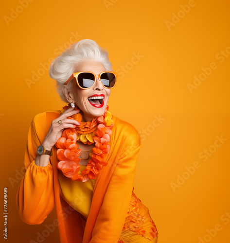 Fancy eldery late 60s grey heir woman funy pink glasses red lipstick happy laughing on the orange wall background. Elderly happy people and calm finance positive retirement concept image. photo