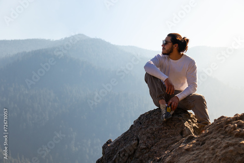 Young man sitting on cliff near foggy mountains photo