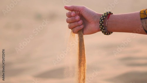 Close up shot of hand pouring desert sand at Khuri sand dunes in Thar desert at Rajasthan, India. Indian Female hand playing with sand, releasing dropping sand. Travel and holidays concept. photo