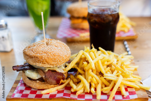 Two double cheeseburgers with bacon and fries on bar with drinks