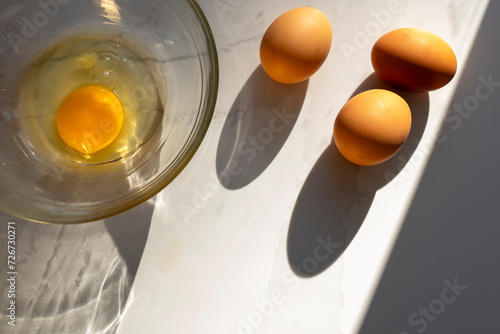 Mixing Bowl with Egg Yolk and Whole Brown Eggs on Kitchen Countertop photo