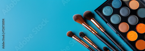 Colorful eyeshadow palette and professional makeup brushes on a blue background. Beauty and makeup concept with copy space for cosmetics design and tutorials.
