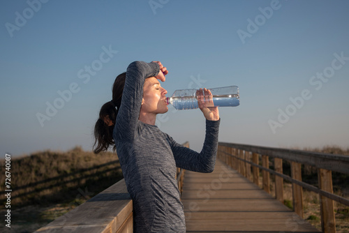Fit, sporty woman drinking water after exercise or running in the heat. Outdoor fitness concept.