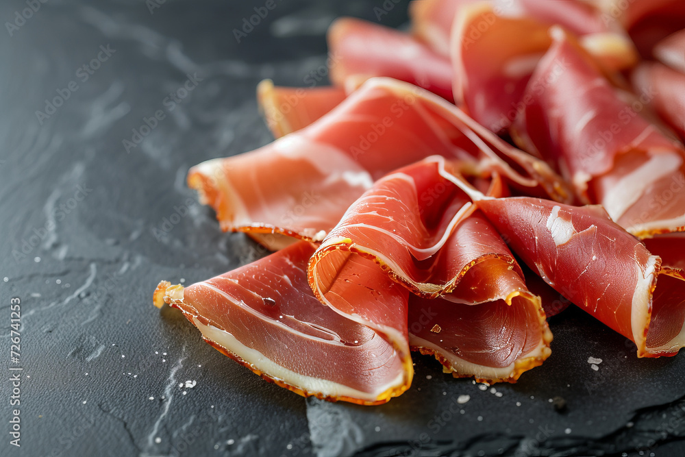 jamon slices, dry italian prosciutto, raw pork ham isolated on black background. Slices of prosciutto di parma or jamon on a black plate on a dark slate, stone or concrete background.