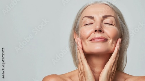 Gorgeous senior older woman with closed eyes touching her perfect skin. Beautiful portrait mid 50s aged woman advertising facial antiage lift products salon care tighten skin isolated on white.