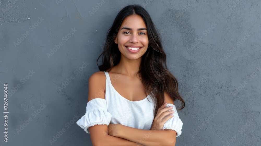 Portrait of a young latin woman with pleasant smile and crossed arms isolated on grey wall with copy space. Beautiful girl with folded arms looking at camera against grey wall. Cheerful hispanic woman Portrait of a young latin woman with pleasant smile and crossed arms isolated on grey wall with copy space. Beautiful girl with folded arms looking at camera against grey wall. Cheerful hispanic woman