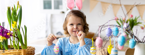 Canvas Print Portrait of cute pretty smiling little girl in blue dress and bunny rabbit ears preparing easter table decor