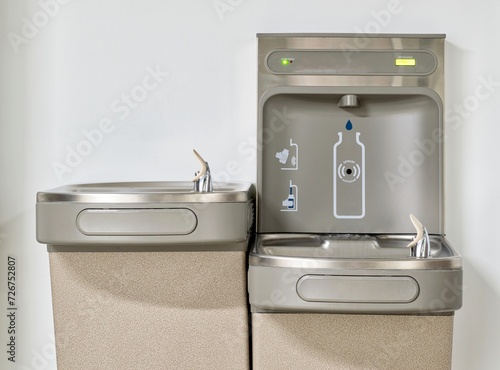 Water bottle refilling station with twin drinking fountains isolated by a plain white wall. Touchless automated eco friendly technology.