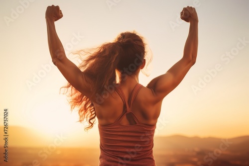 Motivated woman with raised arms celebrating success in sunset light, symbolizing fitness goals and empowerment photo
