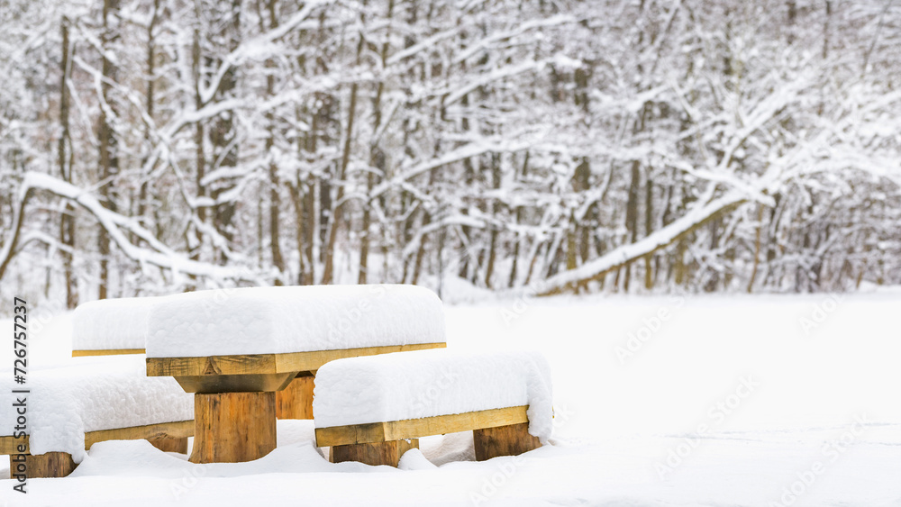 Wooden benches and tables covered with a thick layer of snow, a resting place in a clearing in front of the forest, a winter landscape with white snow. Wooden benches and tables covered with a thick layer of snow, a resting place in a clearing in front of the forest, a winter landscape with white snow.