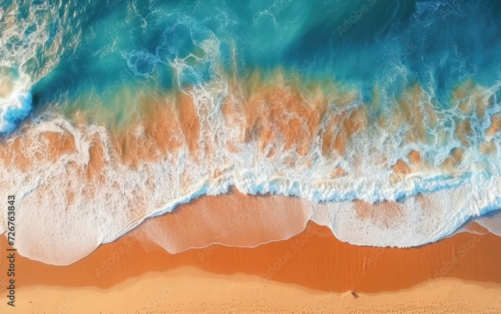Aerial plan view of waves kissing the sandy shore. A dance of colors and textures, embodying the serene meeting of land and sea
