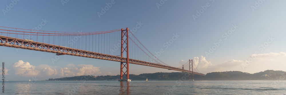 Fototapeta premium Panorama of red bridge 25 de Abril Bridge and statue of Cristo Rei during a slightly misty day, Lisbon, Portugal