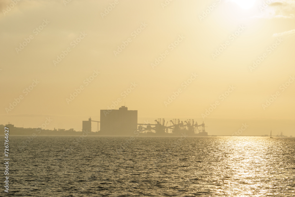 Terminal Portuario da Trafaria the port of Trafaria with cranes in the hazy distance during golden sunset, Lisbon, Portugal Terminal Portuario da Trafaria the port of Trafaria with cranes in the hazy distance during golden sunset, Lisbon, Portugal