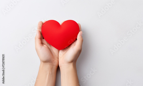 Male hand holding red paper heart on light background with space for text.