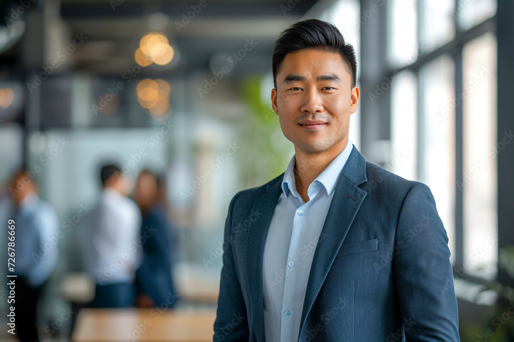 Portrait of a handsome smiling Asian businessman boss in a suit standing in a modern business company office Portrait of a handsome smiling Asian businessman boss in a suit standing in a modern business company office