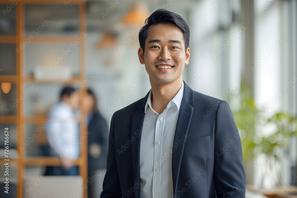 Portrait of a handsome smiling Asian businessman boss in a suit standing in a modern business company office Portrait of a handsome smiling Asian businessman boss in a suit standing in a modern business company office