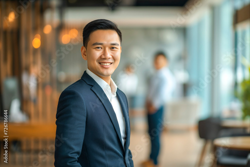 Portrait of a handsome smiling Asian businessman boss in a suit standing in a modern business company office
