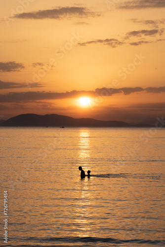 Figures of a man and a boy walking into the water in the sunset