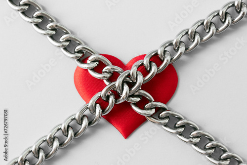 Red heart and metal chains. Minimal concept of domination, manipulation and abuse in relations. Selective focus, copy space