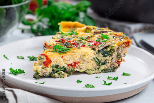 Piece of egg frittata with spinach, roasted peppers, mushrooms, cheese, on plate, horizontal closeup