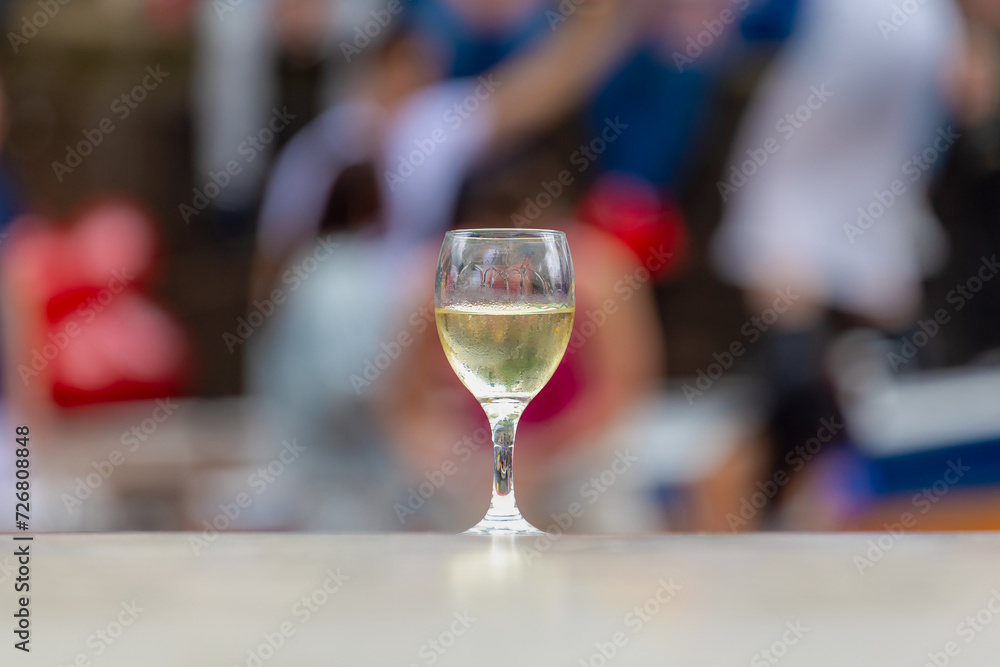 Drink and beverage concept, Selective focus a glass of white wine on the table with blurred peoples as background, Outdoor cetaring party and meeting in summer.