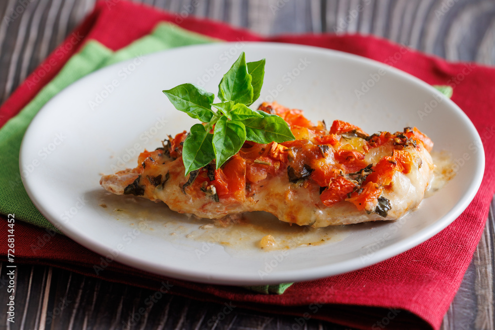 Grilled chicken breast with tomato and mozzarella cheese on it. On plate on wooden table with red and green napkins Grilled chicken breast with tomato and mozzarella cheese on it. On plate on wooden table with red and green napkins