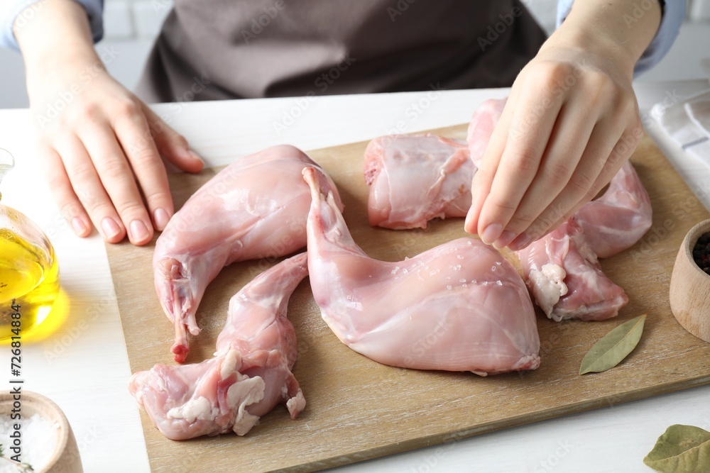 Woman putting salt onto raw rabbit meat at white wooden table, closeup