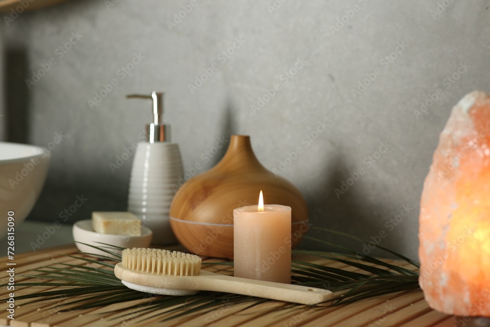 Composition with different spa products, burning candle and Himalayan salt lamp on countertop in bathroom