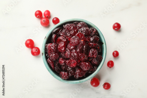 Tasty dried cranberries in bowl and fresh ones on white table, top view photo