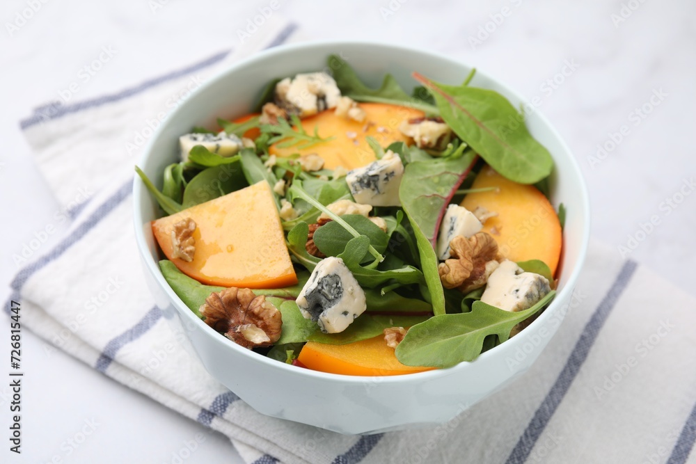 Tasty salad with persimmon, blue cheese and walnuts served on white table Tasty salad with persimmon, blue cheese and walnuts served on white table