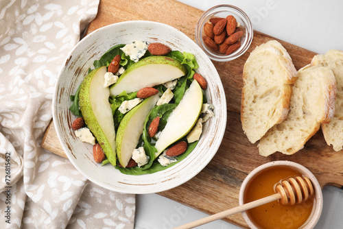 Delicious pear salad in bowl, honey and bread on light table, top view photo