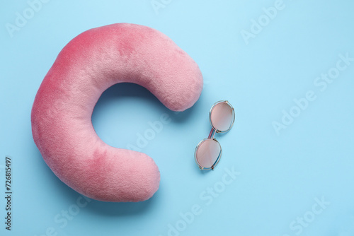 Pink travel pillow and sunglasses on light blue background, flat lay. Space for text