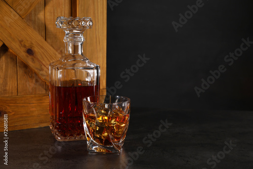 Whiskey in glass and bottle near wooden crate on dark table against black background. Space for text