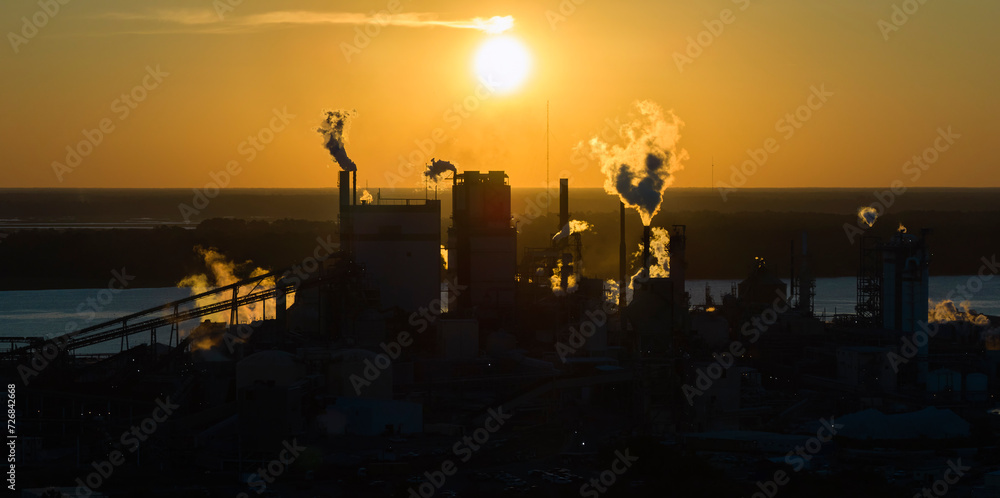 Large factory structure with smoke from production process rising up polluting atmosphere at manufacturing yard. Industrial site at sunset Large factory structure with smoke from production process rising up polluting atmosphere at manufacturing yard. Industrial site at sunset