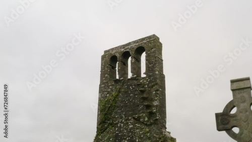 Moss lichen covered church tower and arch windows with eerie old graveyard headstones photo