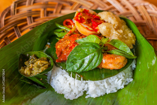 Rice with various side dishes in it, usually called nasirames in Indonesia. served in a place made of babu and covered with banana leaves photo