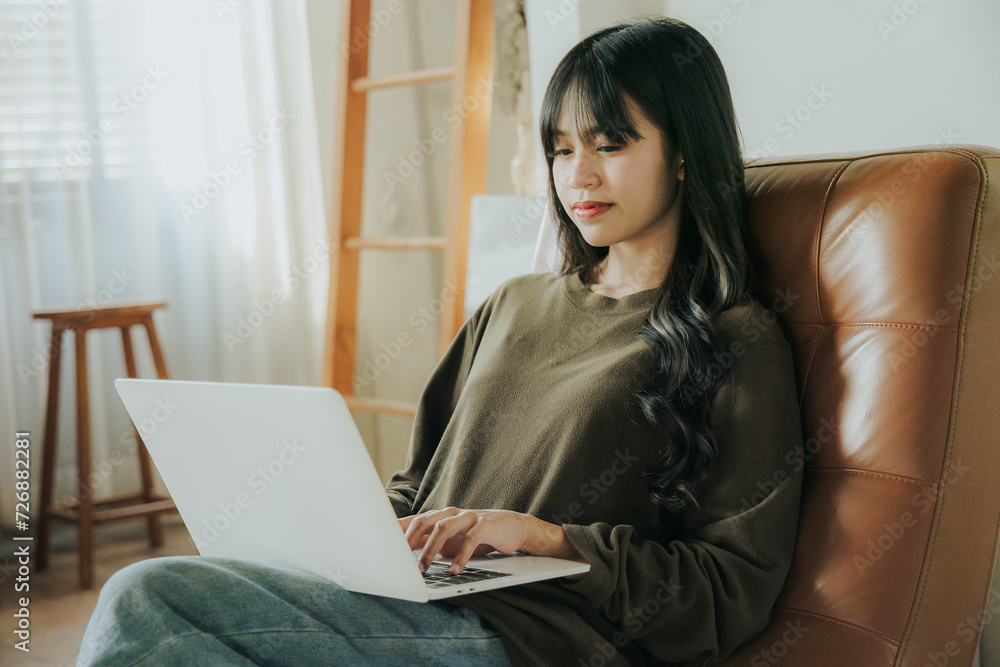 Young Asian woman sitting at desk using laptop as her work tool in cafe or at home. Young Asian woman sitting at desk using laptop as her work tool in cafe or at home.