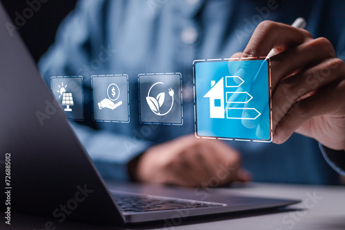 Energy efficiency concept. Businessman use laptop with virtual screen of energy efficiency rating for energy efficient house building rate label audit. photo