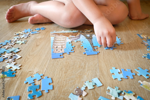 Isolated pieces of puzzle on the floor with kid's hand trying to solve it